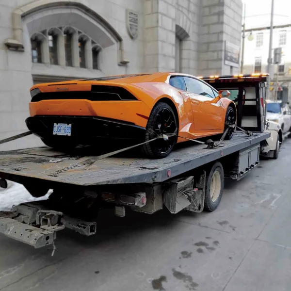 Metro FB-10 flatbed towing an orange Lamborghini supercar in the city
