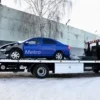 Metro FB-10 flatbed tow truck transporting a blue sedan in winter conditions