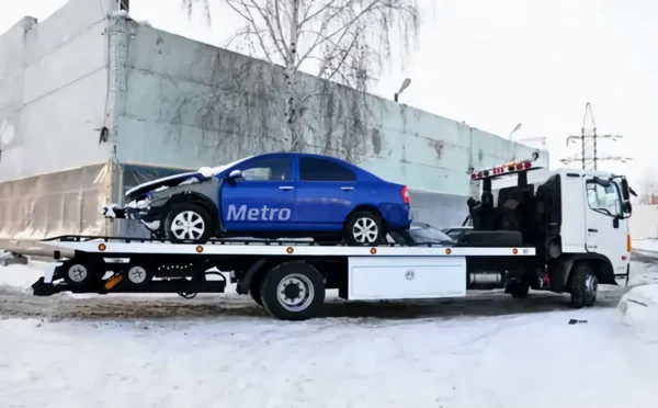 Metro FB-10 flatbed tow truck transporting a blue sedan in winter conditions
