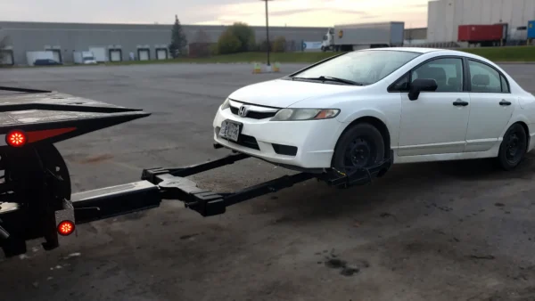 Metro FB-15 flatbed tow truck using wheel lift to tow a white sedan