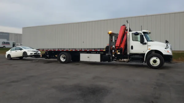Metro FB-15 flatbed tow truck using wheel lift to tow a white sedan