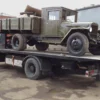 Metro FB-15 flatbed tow truck transporting a vintage military truck on deck