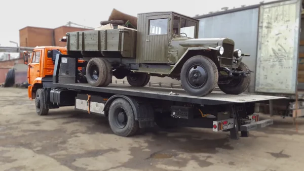Metro FB-15 flatbed tow truck transporting a vintage military truck on deck
