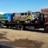 Metro FB-15 flatbed hauling a van and a truck in an industrial yard
