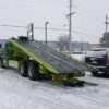 Metro FB-20 lime-green flatbed tow truck loading position in snowy parking lot with deck fully inclined