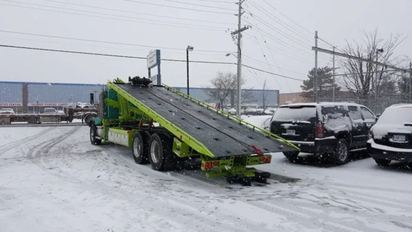 Metro FB-20 lime-green flatbed tow truck loading position in snowy parking lot with deck fully inclined