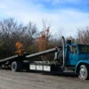 Metro FB-20 tilt-and-slide flatbed tow truck with extended deck in rural yard setting