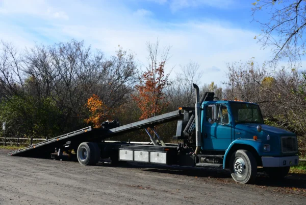 Metro FB-20 tilt-and-slide flatbed tow truck with extended deck in rural yard setting