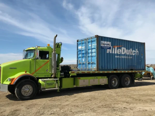 Metro FB-20 long-deck flatbed truck carrying a shipping container on job site