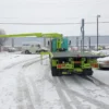 Metro FB-20 flatbed tow truck operating in snowy yard with knuckle crane rotating and extending