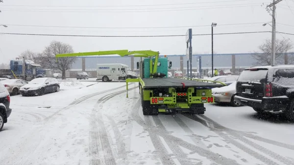 Metro FB-20 flatbed tow truck operating in snowy yard with knuckle crane rotating and extending
