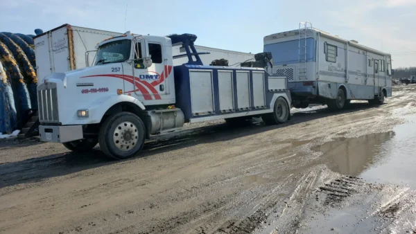 Metro Tow Trucks INT-16 white heavy-duty integrated wrecker left side profile towing a bus on muddy ground in industrial area