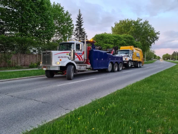 INT-60 heavy duty integrated wrecker towing a garbage truck along a rural roadway