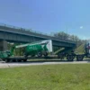 TSA-50 low-profile trailer transporting a green agricultural conveyor machine beneath an overpass