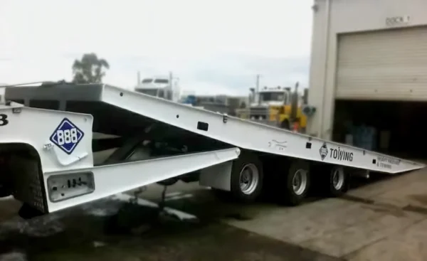 Side view of a TSA-50 tilt deck trailer partially lowered at a warehouse loading bay