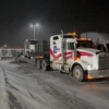 TSA-50 trailer hauling a tractor truck during nighttime on a snowy road