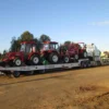 TSA-50 heavy-duty flatbed trailer carrying multiple farm tractors across a gravel yard