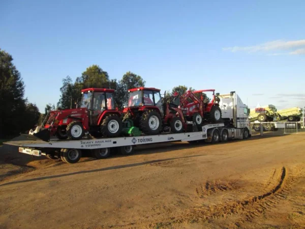 TSA-50 heavy-duty flatbed trailer carrying multiple farm tractors across a gravel yard