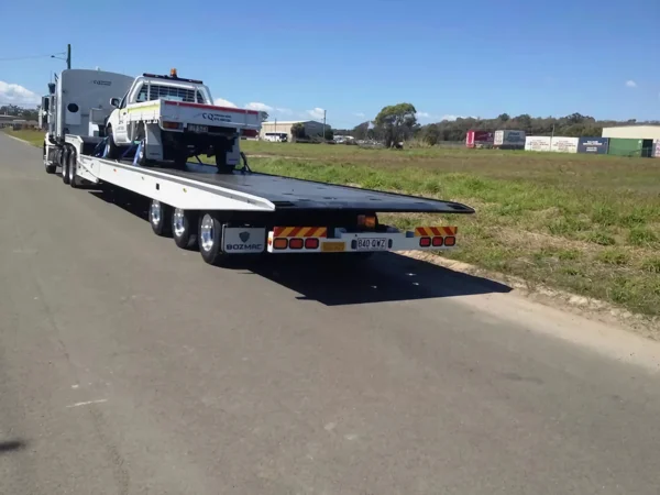 Side view of TSA-50 trailer unloading a light-duty tow truck on a roadside shoulder