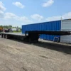 STT-50 extendable trailer parked in yard with shipping containers, showing full-length deck and axle spacing