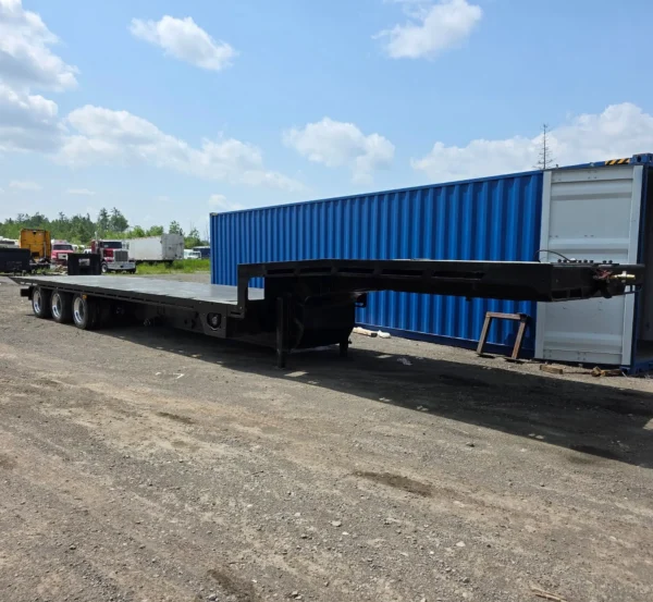 STT-50 extendable trailer parked in yard with shipping containers, showing full-length deck and axle spacing