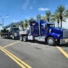 Blue MDTU-20 detachable tow truck transporting a crane truck on highway with palm trees in background