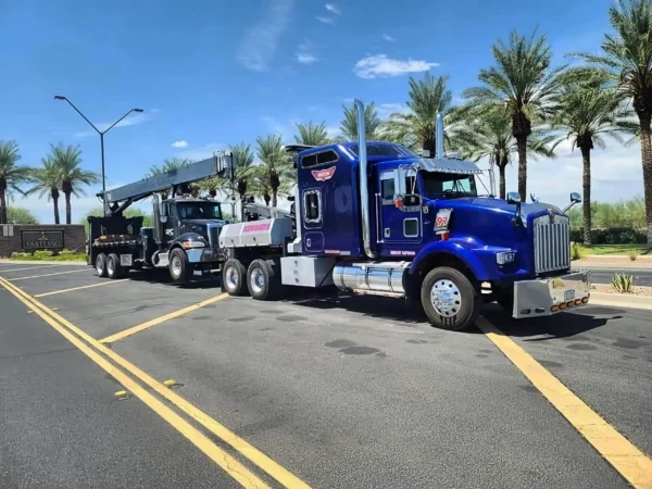 Blue MDTU-20 detachable tow truck transporting a crane truck on highway with palm trees in background